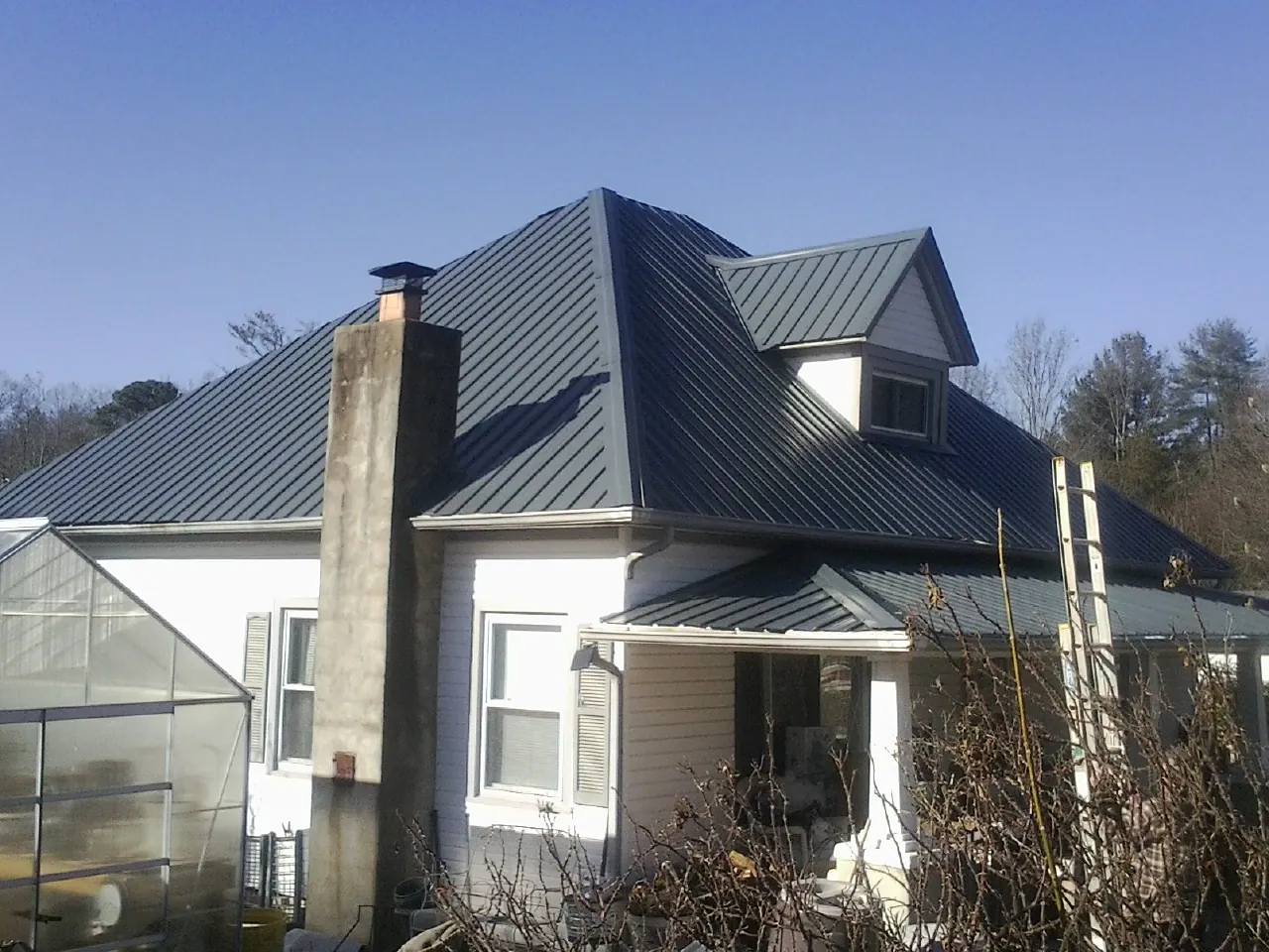 Dark blue standing seam metal roof on a white farmhouse with dormer — Slate & Tile Roof Repair by Roofing Brothers in Manvel