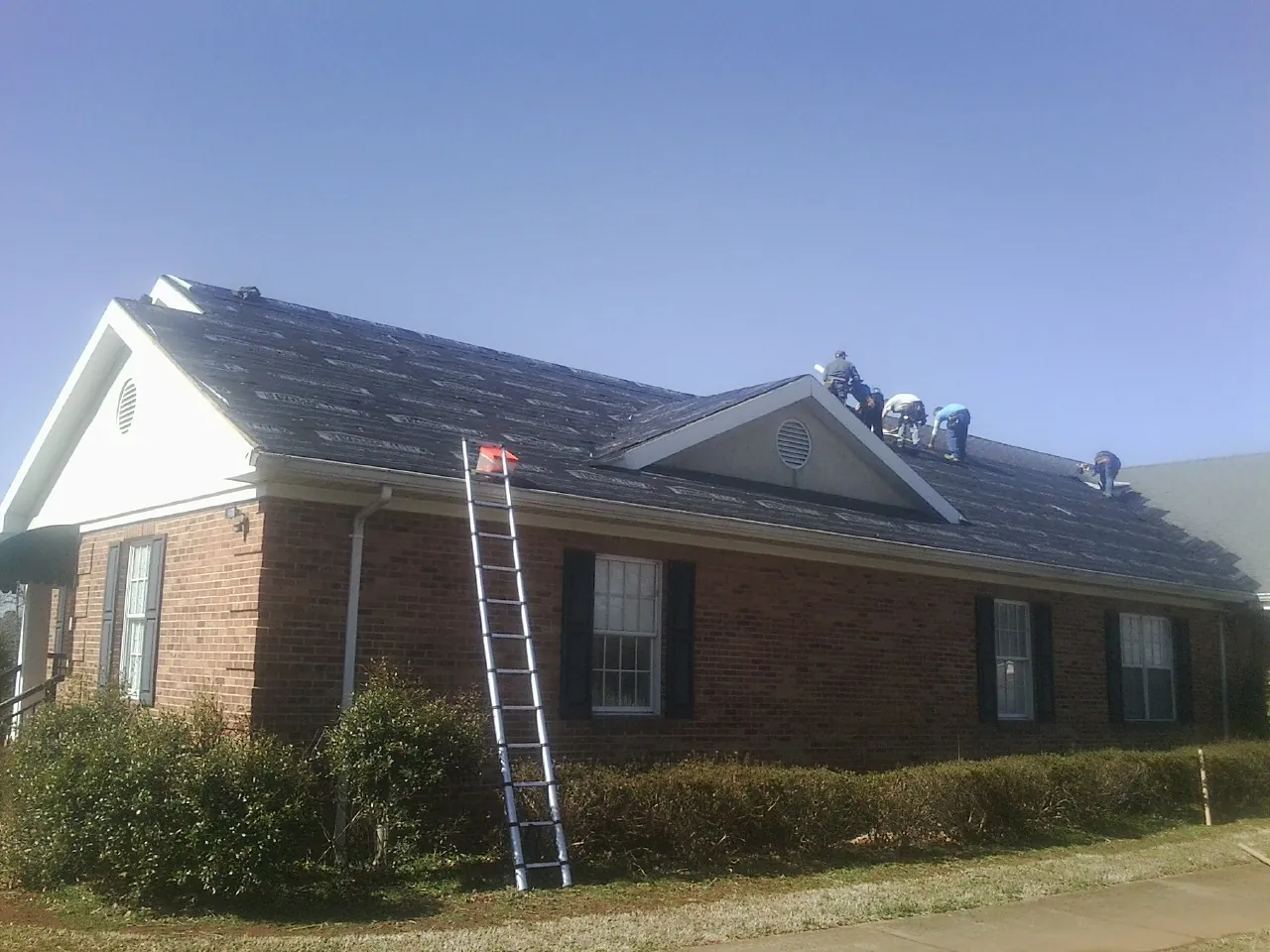 Crew tearing shingles off a brick ranch roof with a ladder set — Emergency Roof Repair work by our crew in Manvel