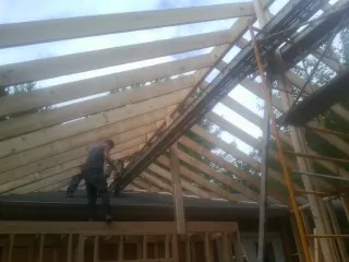 Rafters going up over a new addition with a worker on the wall in Manvel