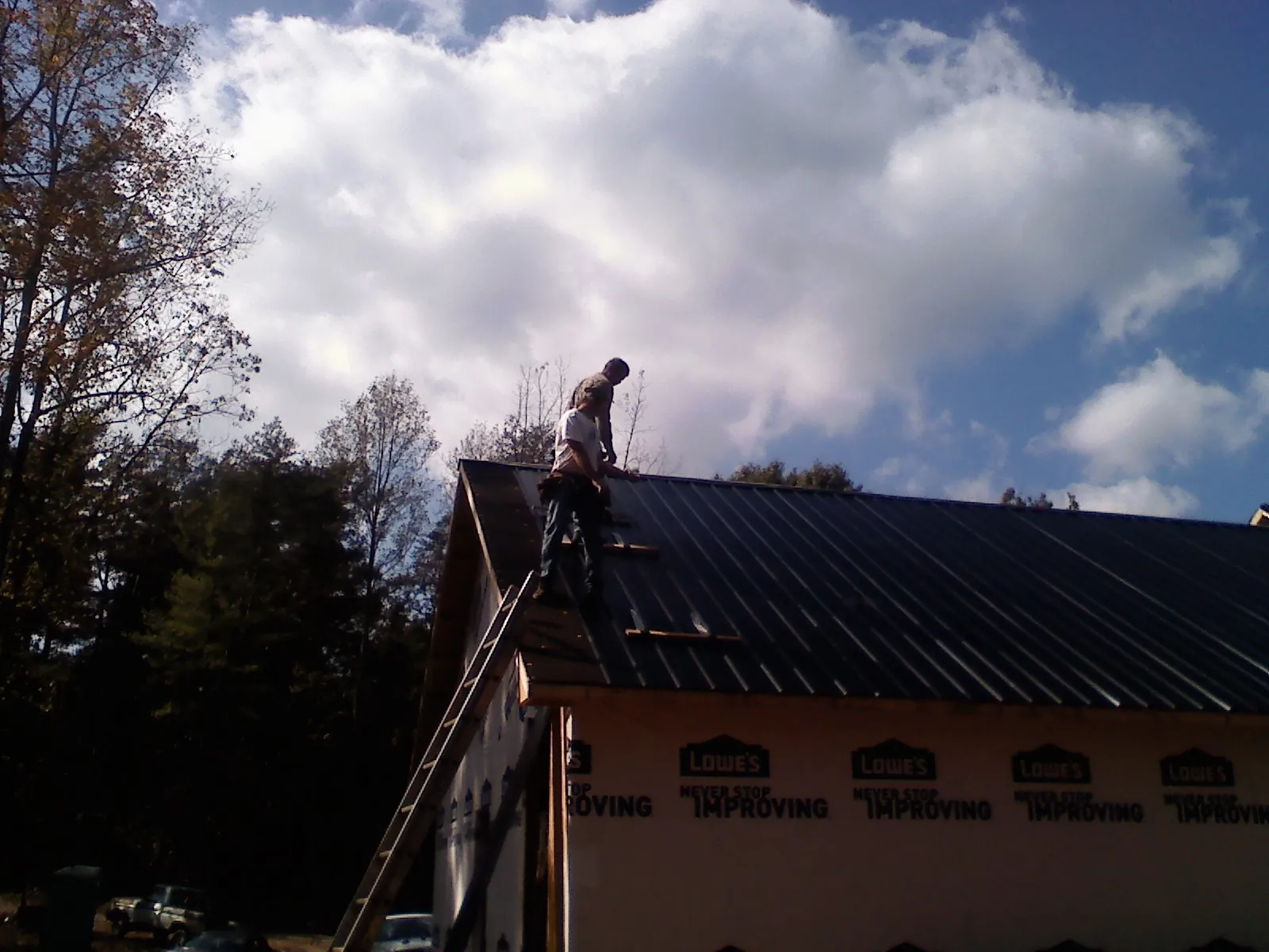 Roofer fastening dark metal panels high against a cloudy sky, from a Roof Inspection job in Manvel