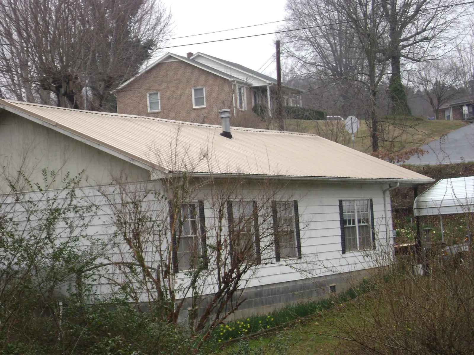 Tan metal roof on a white sided house set into a hillside — Commercial Roofing by Roofing Brothers in Manvel