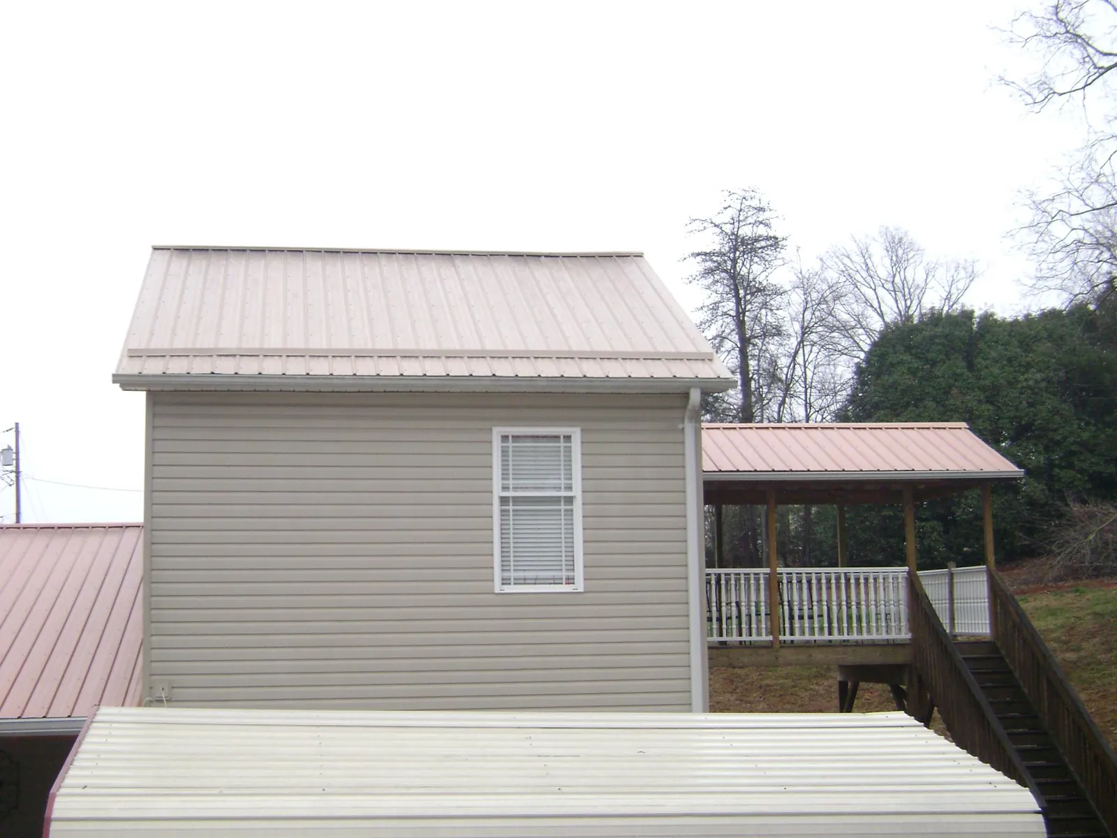 Tan metal roofs on a two story addition and attached porch, from a Roof Replacement job in Manvel