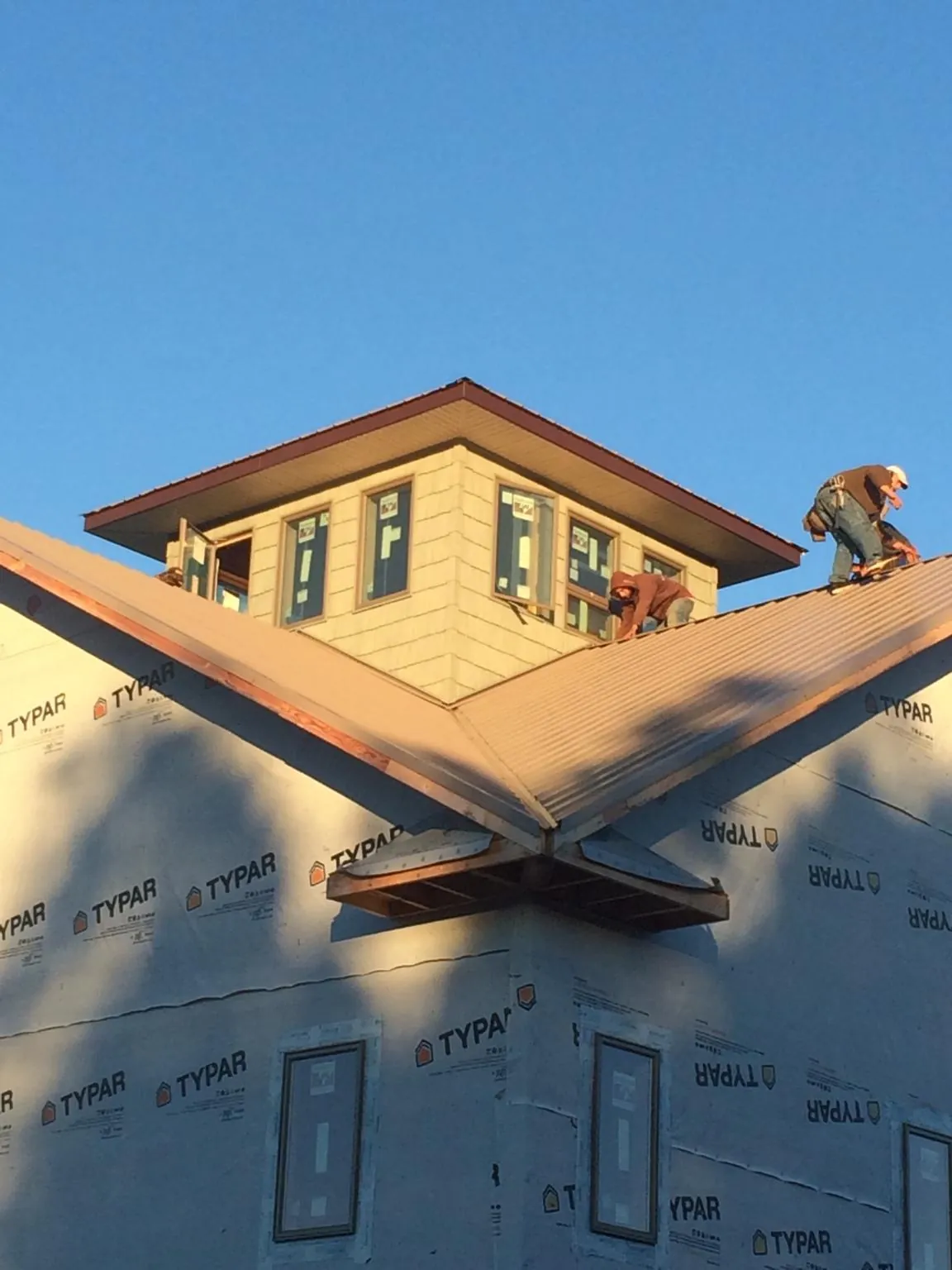Roofers working around a rooftop cupola on a new metal roof at sunset — Roof Waterproofing in Manvel by Roofing Brothers